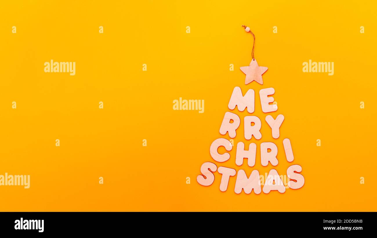 Text Frohe Weihnachten in Form von Tannenbaum aus Holzbuchstaben auf orangefarbenem Hintergrund Stockfoto