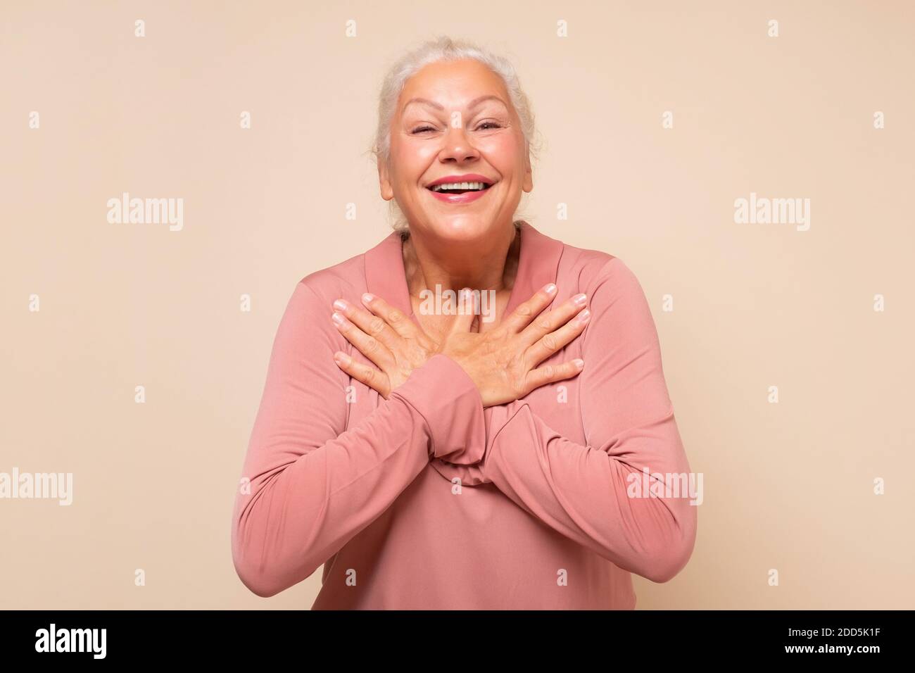 Ältere Frau immer Komplimente frisch aussehen. Entzückte glücklich charmante alte Dame mit weißen Haaren hält Palmen auf Herz Stockfoto