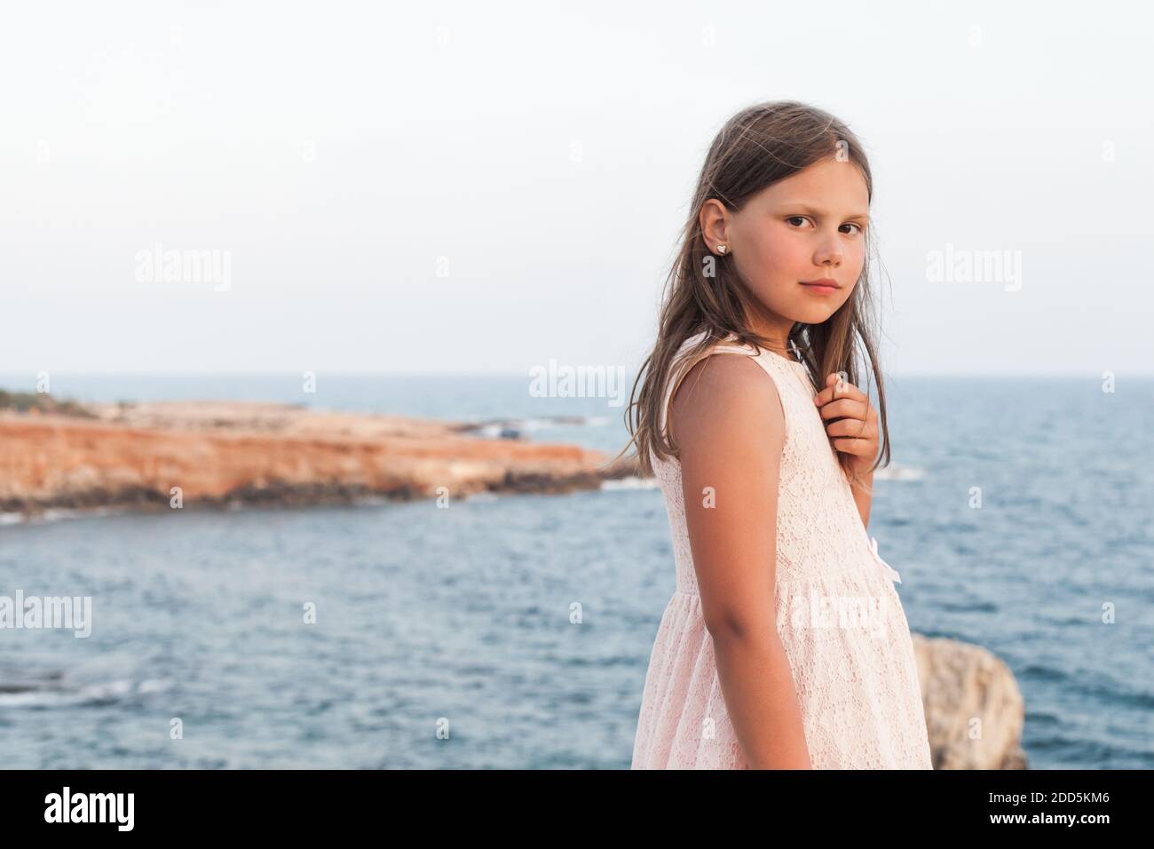 Kleines Mädchen in weißem Kleid steht an der Küste, Outdoor-Porträt mit weichen selektiven Fokus Stockfoto