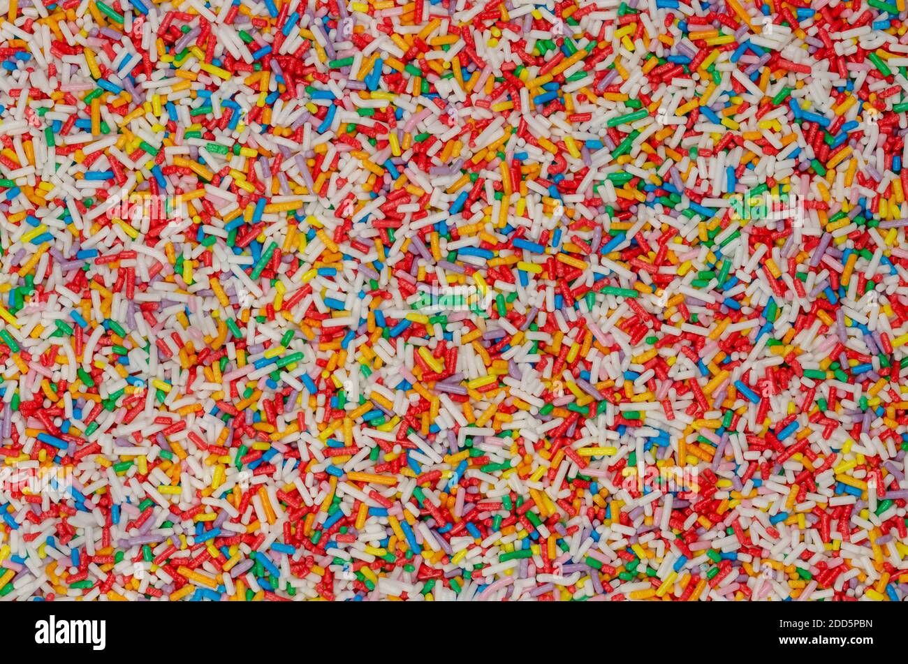 Regenbogen-Streuseln, Hintergrund und Oberfläche. Stangenförmige bunte Zuckerstreuseln. Kleine Bonbons in verschiedenen Farben, als Dekoration oder Topping verwendet. Stockfoto