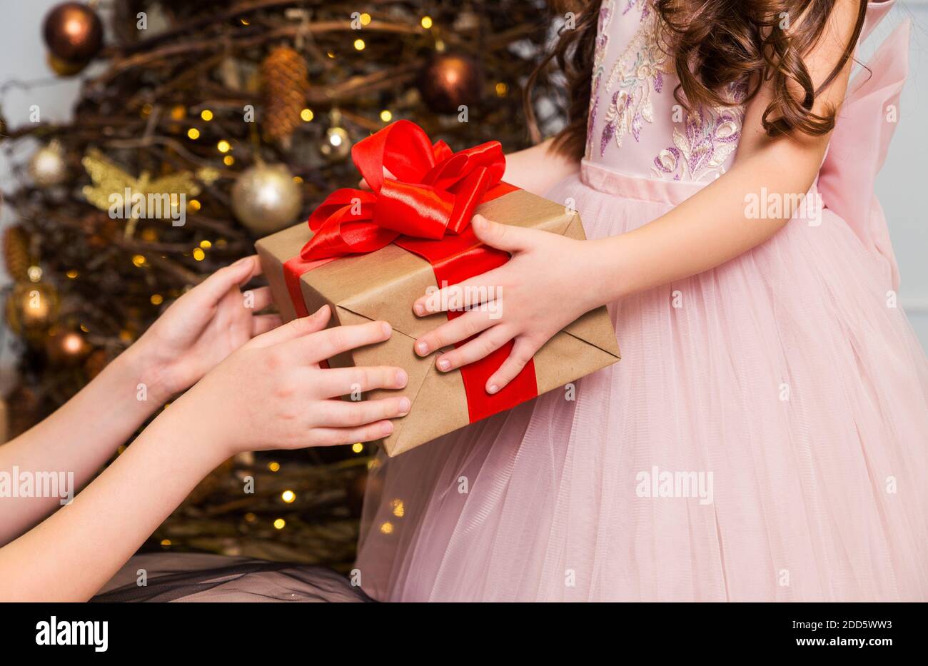 Weibliche Hände halten einem kleinen Mädchen eine Geschenkbox mit roter Schleife vor Stockfoto