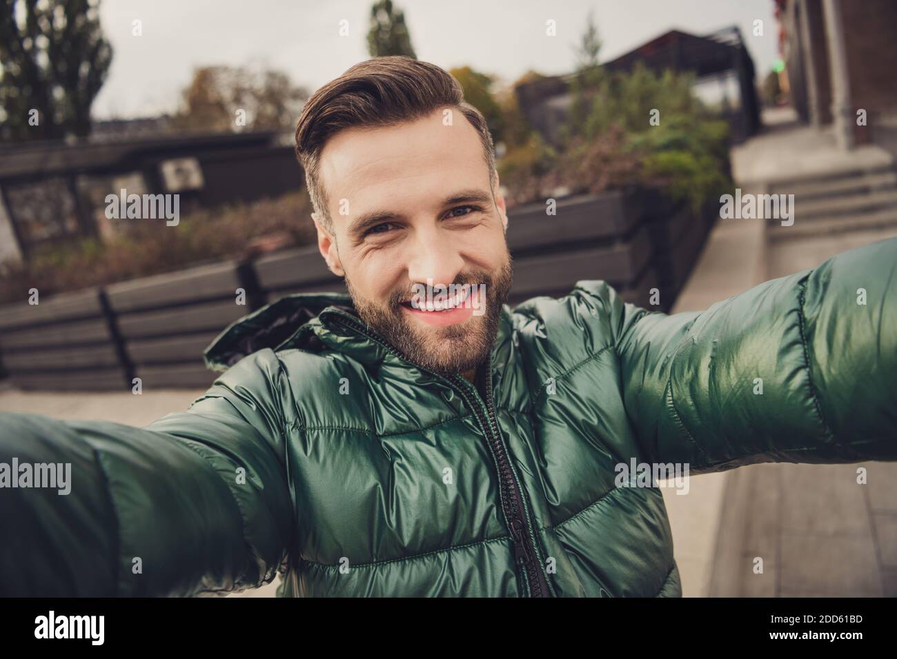 Foto von charmanten schönen jungen Mann tragen grüne Windbreaker machen Selbstvideo außerhalb der Stadtstraße Stockfoto