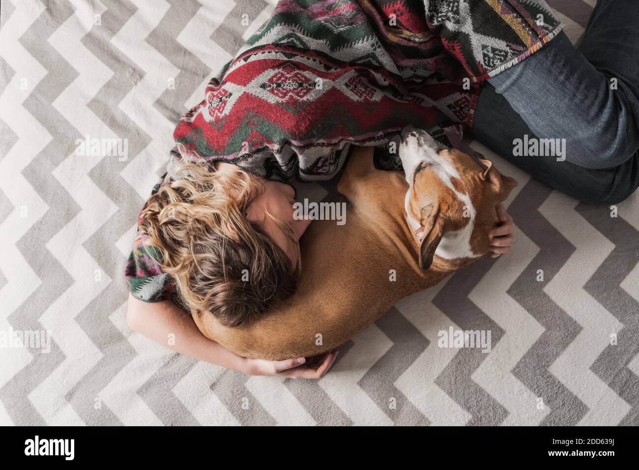 Frau legt sich mit einem Hund hin und umarmt sie. Emotionale Unterstützung, Depression und Stressabbau mit Haustieren während Lockdown und zu Hause zu bleiben Bestellungen Stockfoto