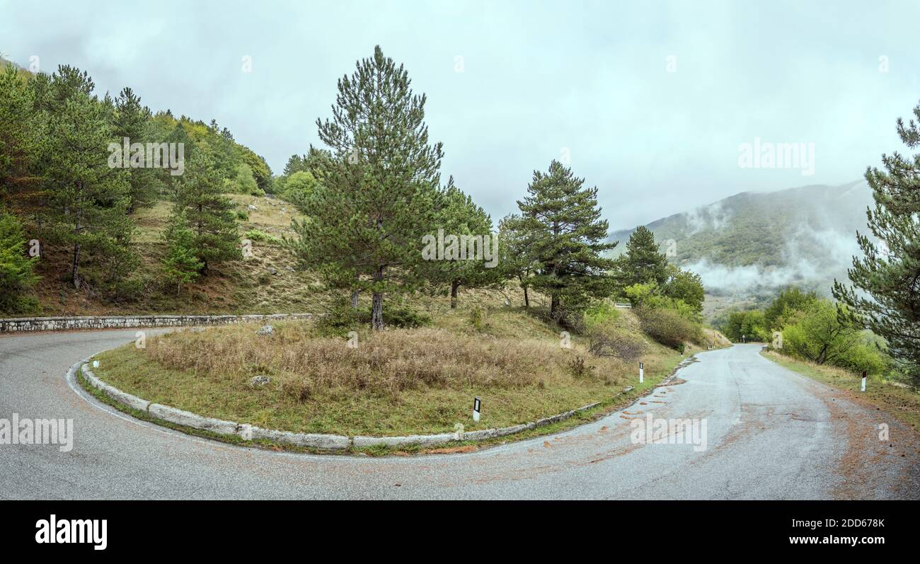 Landschaft mit Bergstraße, die Haarnadelkurve auf grünen Berghängen macht, erschossen unter niedrigen hellen Wolken in der Nähe von Godi Pass, L'Aquila, Abruzzen, Italien Stockfoto