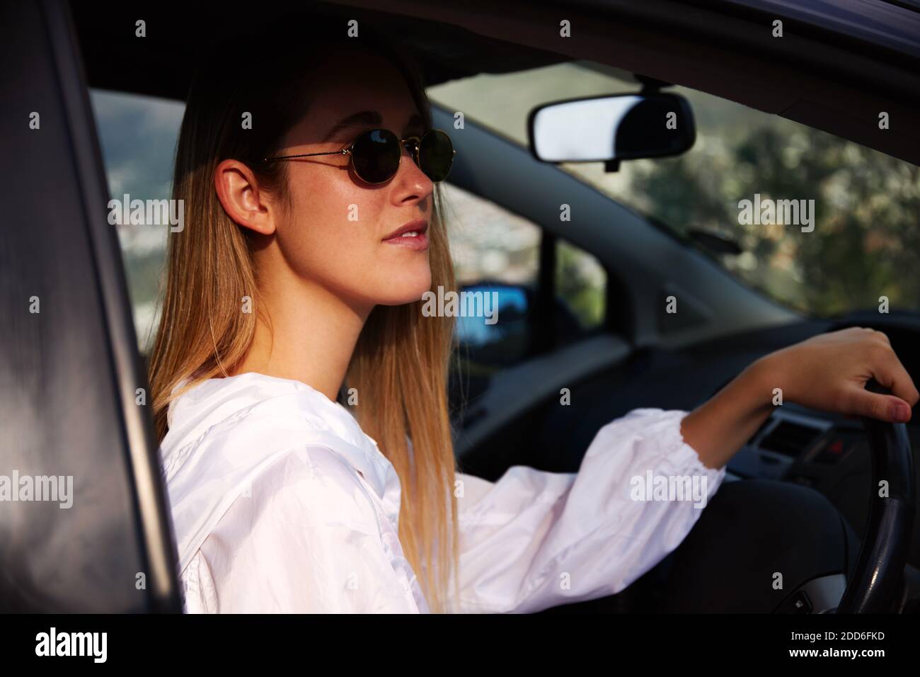 Junge Frau trägt Sonnenbrille hinter dem Lenkrad auf der Straße Reise Urlaub durch offene Tür des Mietwagens Stockfoto
