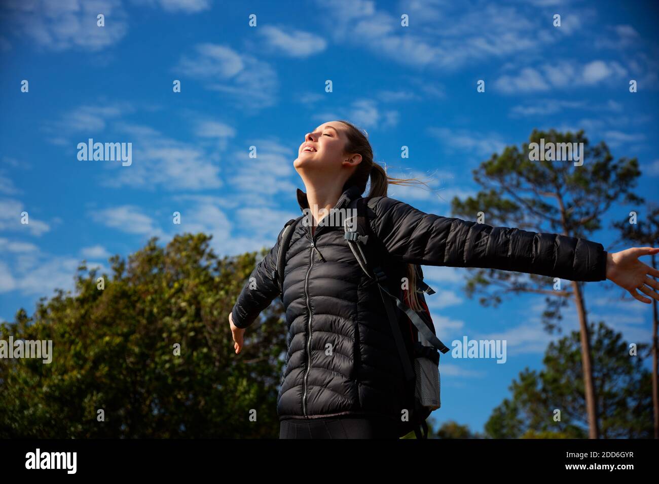 Aktive junge Frau trägt Rucksack auf Wanderung in der Landschaft Verbreitung Ihre Arme und ihre Augen schließen, während sie Sinn genießt Freiheit und Raum Stockfoto