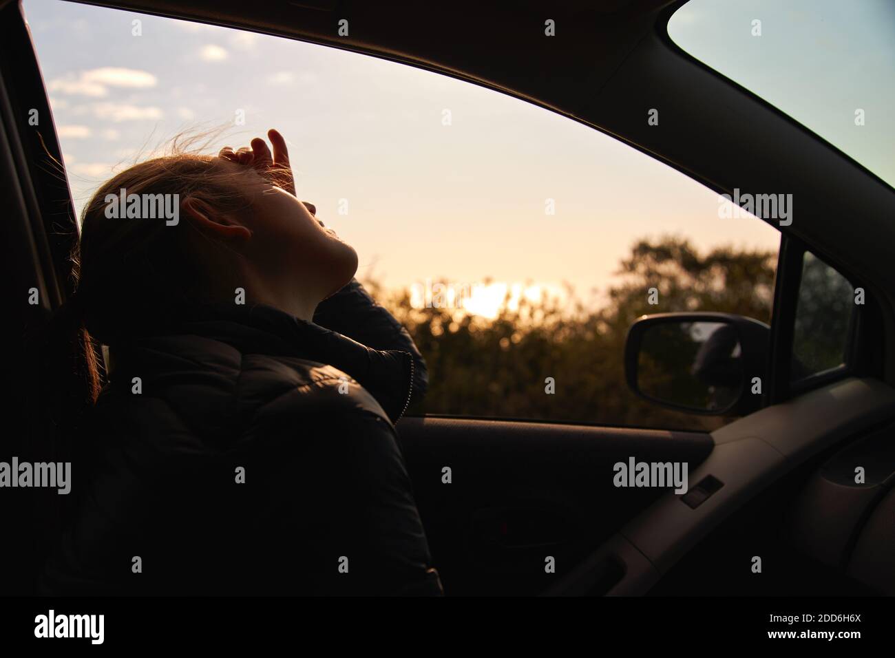 Junge Frau unterwegs Urlaub fahren und schauen Der Mietwagen Fenster als Sonne untergeht Stockfoto