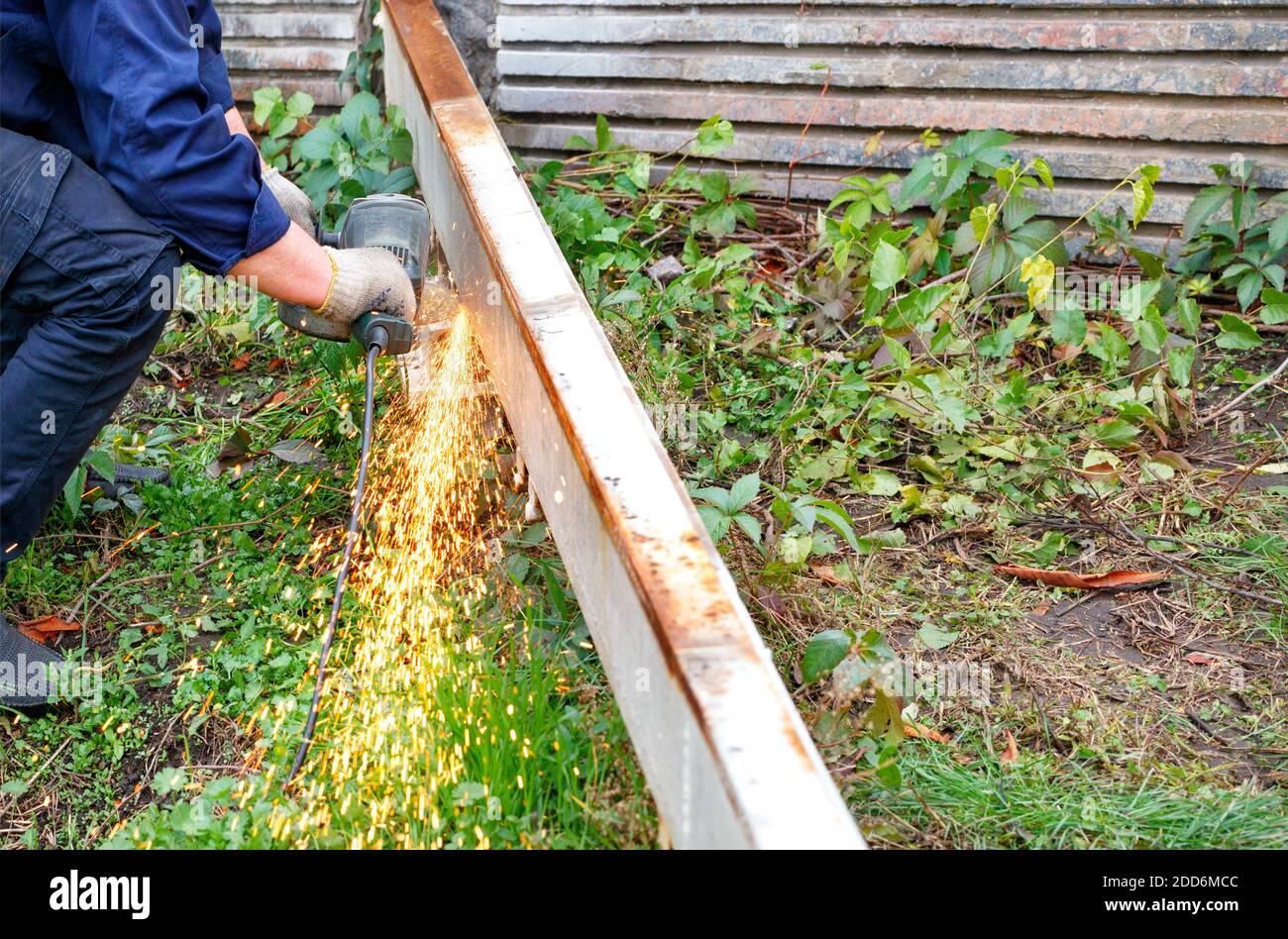 Der Arbeiter schneidet die Metallstruktur mit einem Scheibenwinkelschleifer, wodurch eine helle Wolke von vielen heißen Funken. Stockfoto