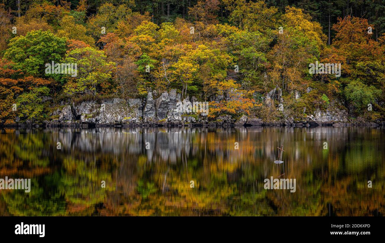 Ein kleines Eisenkreuz im Trossachs Nationalpark reflektiert Im ruhigen Herbstwasser von Loch ARD Stockfoto