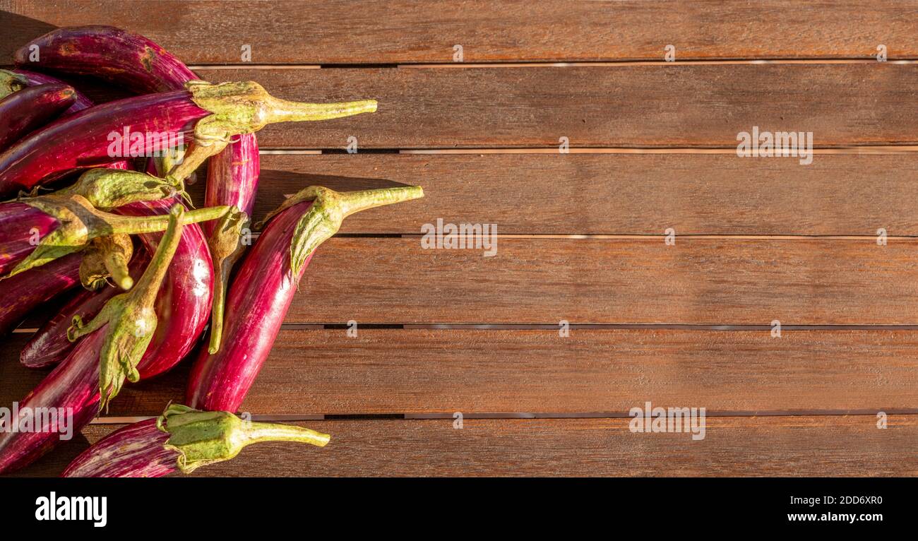 Viele kleine Auberginen liegen auf der linken Seite einer Holzfläche. Sonnenlicht reflektiert auf Essen. Natürliches Gemüse mit Kopierfläche Stockfoto