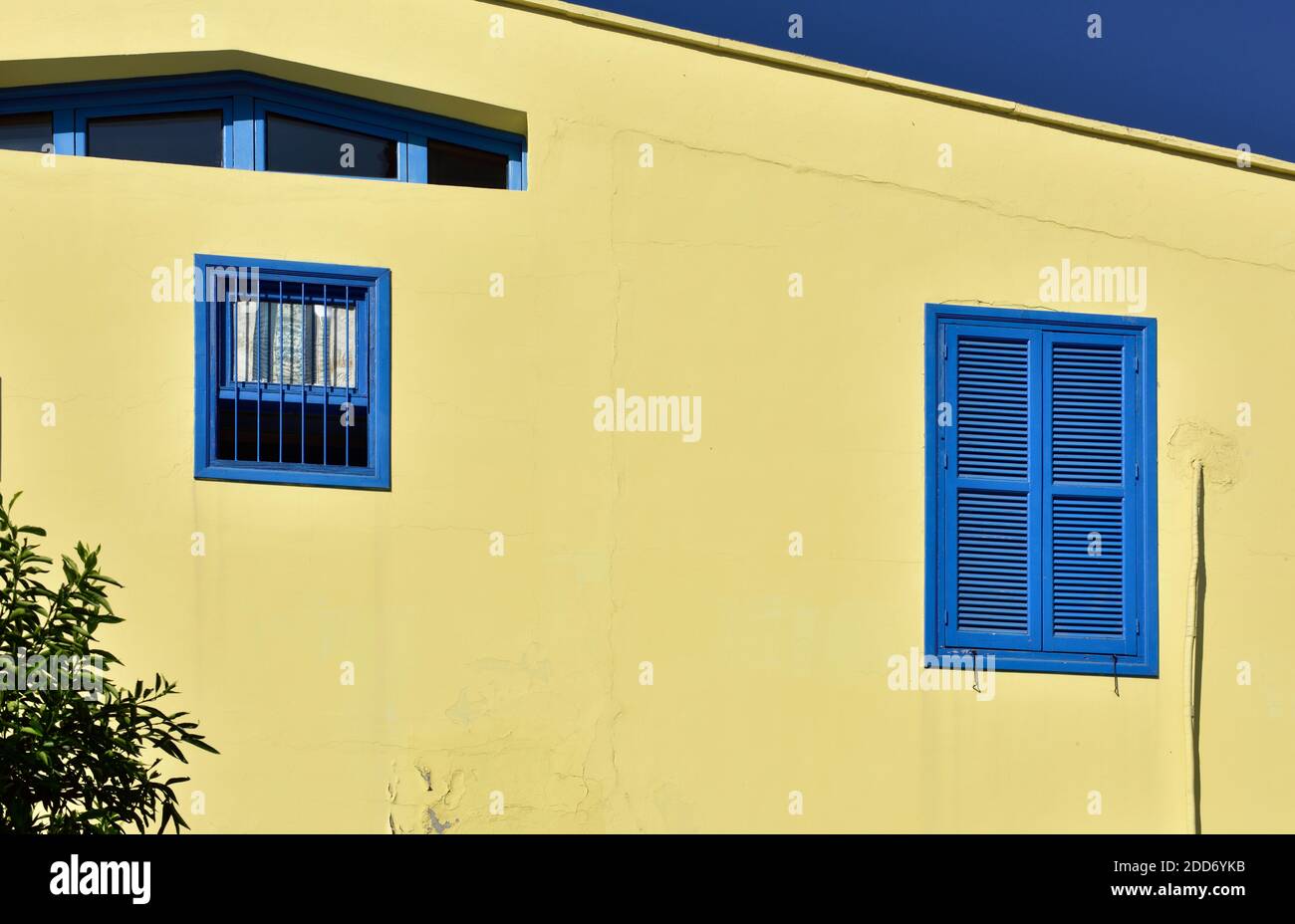 Gelbe Endwand des Hauses mit blauen Fensterläden und Andere blaue Fenster Stockfoto