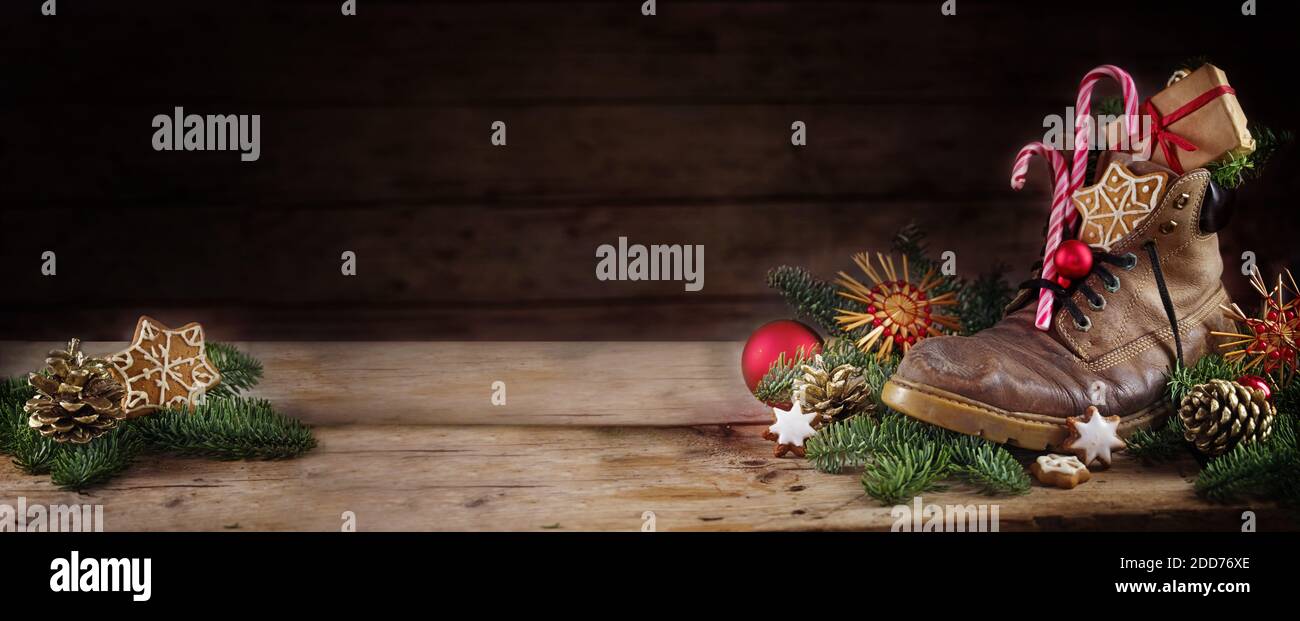 Alte Wanderstiefel gefüllt mit Süßigkeiten, Geschenken und Weihnachtsschmuck, Deutsche Tradition am Nikolaus- oder Nikolaus-Tag am 6. Dezember, dunkel rustikal hölzernes b Stockfoto