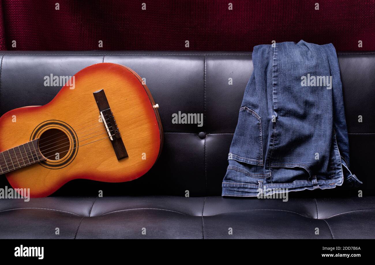 Blaue Jeans und Akustikgitarre auf der Couch mit weichem Deckenlicht. Stockfoto