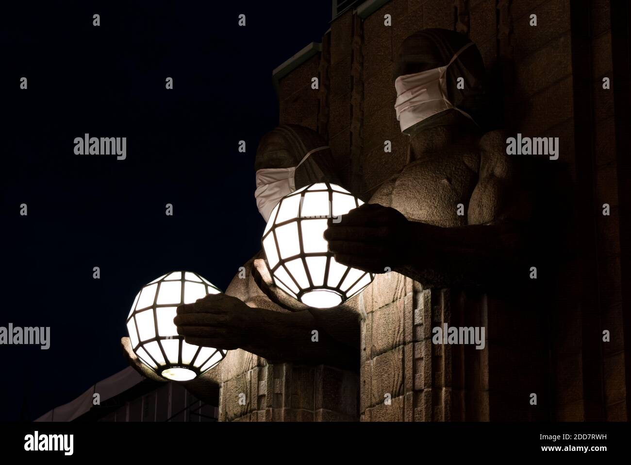 Zwei Statuen, die kugelförmige Lampen halten und Gesichtsmasken tragen Der Eingang zum Hauptbahnhof von Helsinki Stockfoto