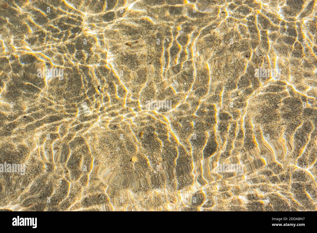 Textur von Meerwasser mit Sand. Trendige hellbeige schillernde Farbe des Meerwassers. Setzen Sie Sail Champagner warmen Meersand in der Sonne. Abstrakt natürliche Rückengr Stockfoto