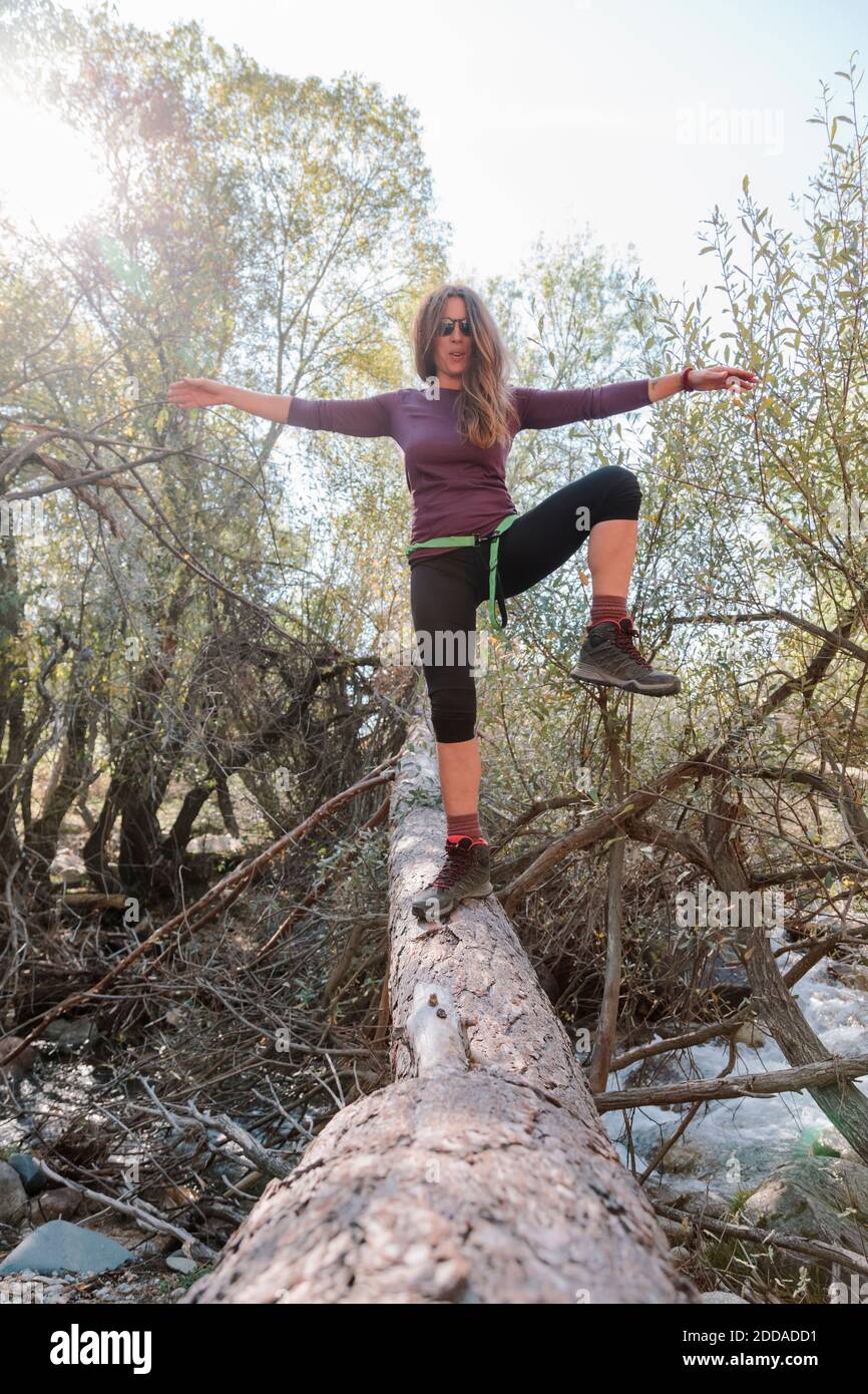 Mittlere Erwachsene Frau, die mit ausgestreckten Armen auf einem gefallenen Baum in La Pedriza, Madrid, Spanien, steht Stockfoto