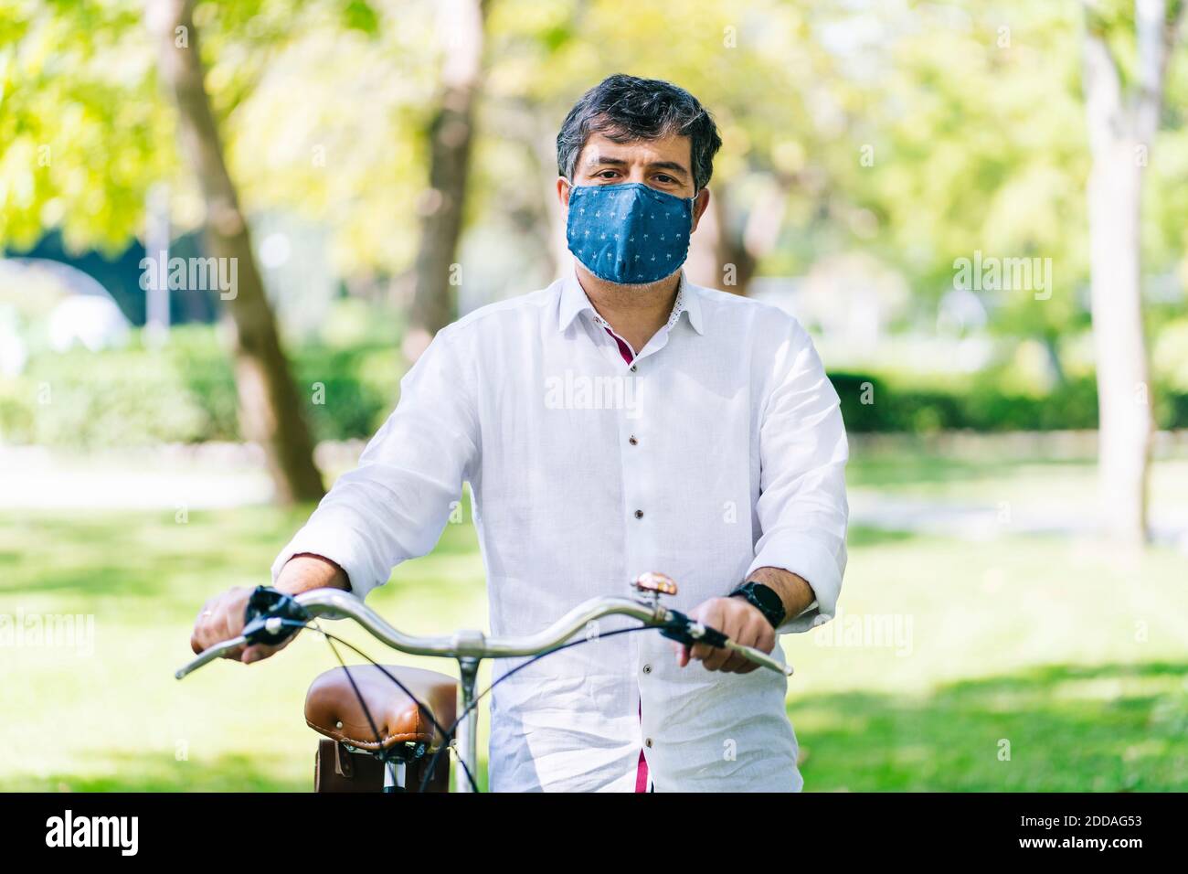 Reifer Mann mit Schutzmaske mit Fahrrad in der Öffentlichkeit parken Sie während der COVID-19 Stockfoto