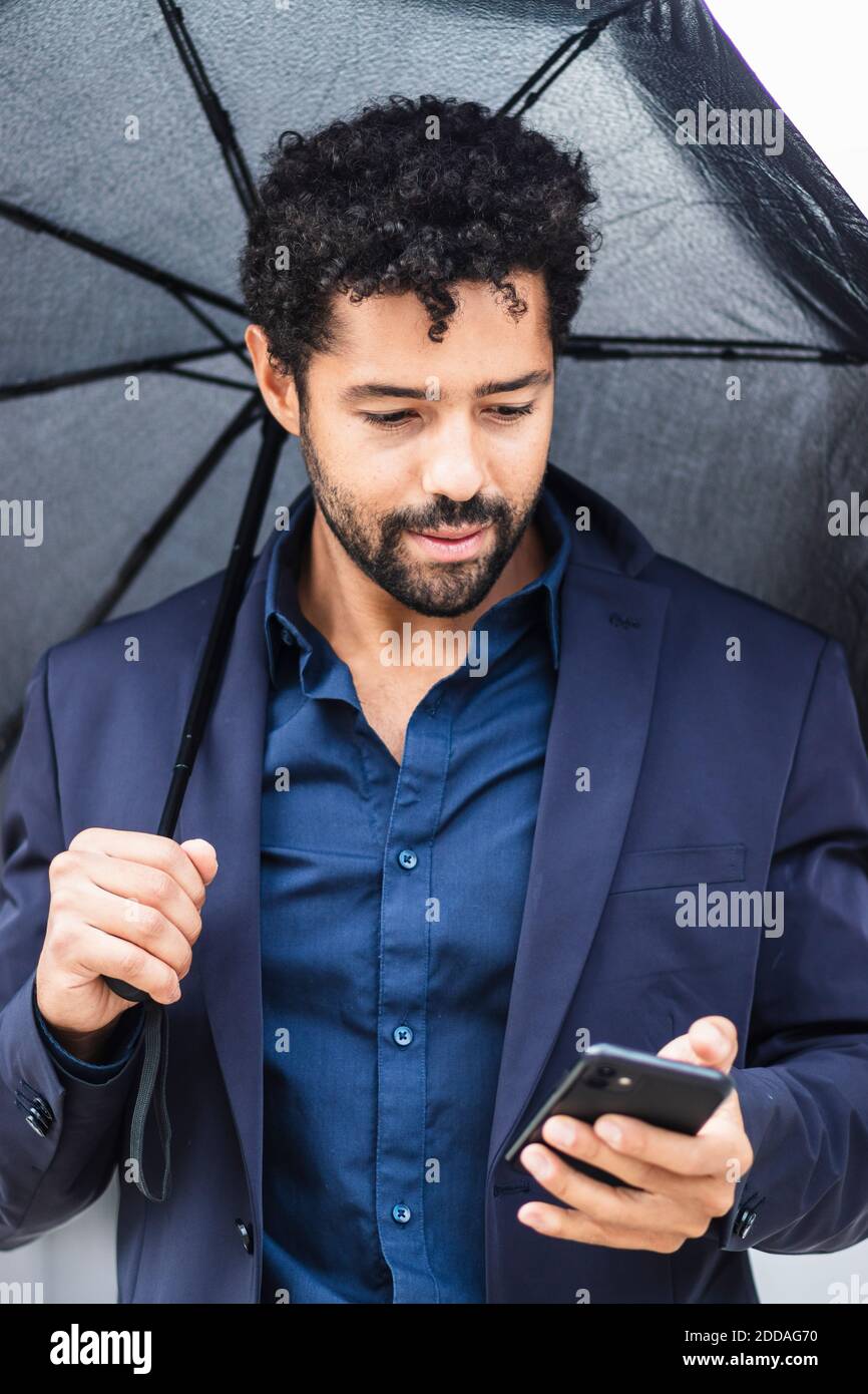 Unternehmer mit Regenschirm mit Smartphone in der Stadt Stockfoto