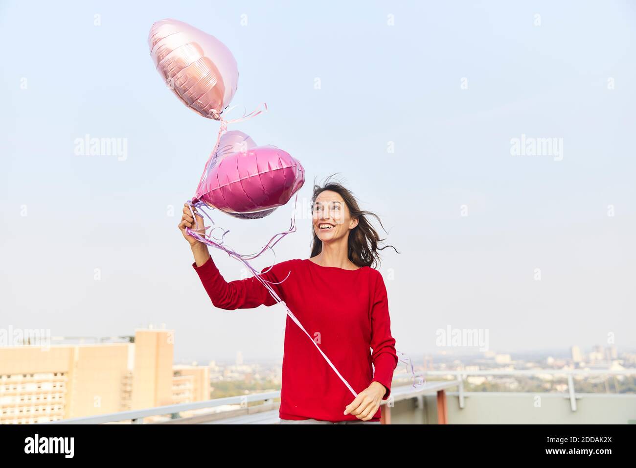 Frau, die Ballon anschaut, während sie auf der Terrasse steht Der Himmel ist klar Stockfoto
