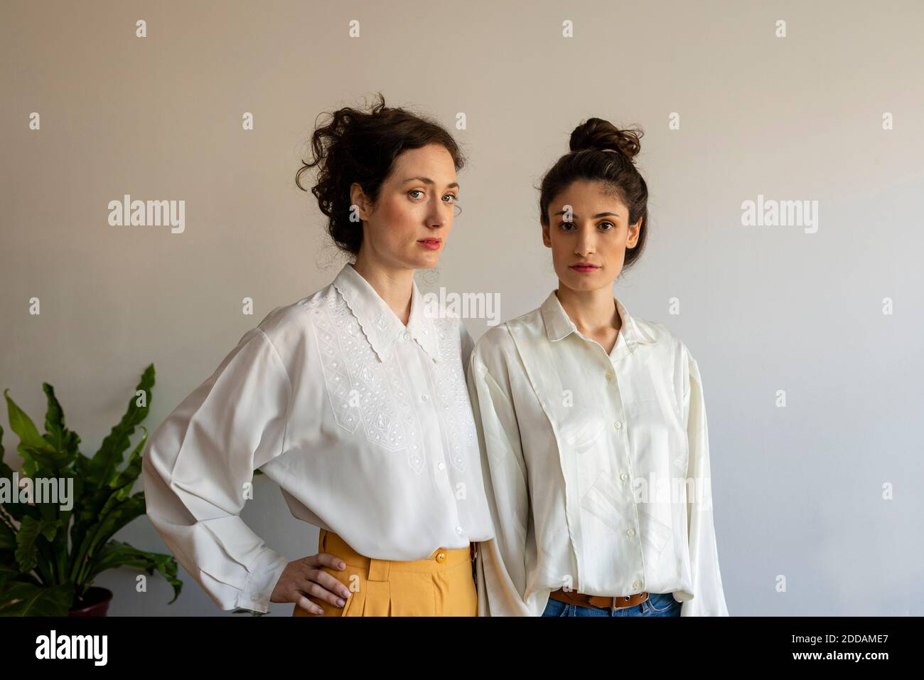 Freundinnen tragen weißes Hemd, das zu Hause gegen die Wand steht Stockfoto Freundinnen tragen weißes Hemd, das zu Hause gegen die Wand steht Stockfoto
