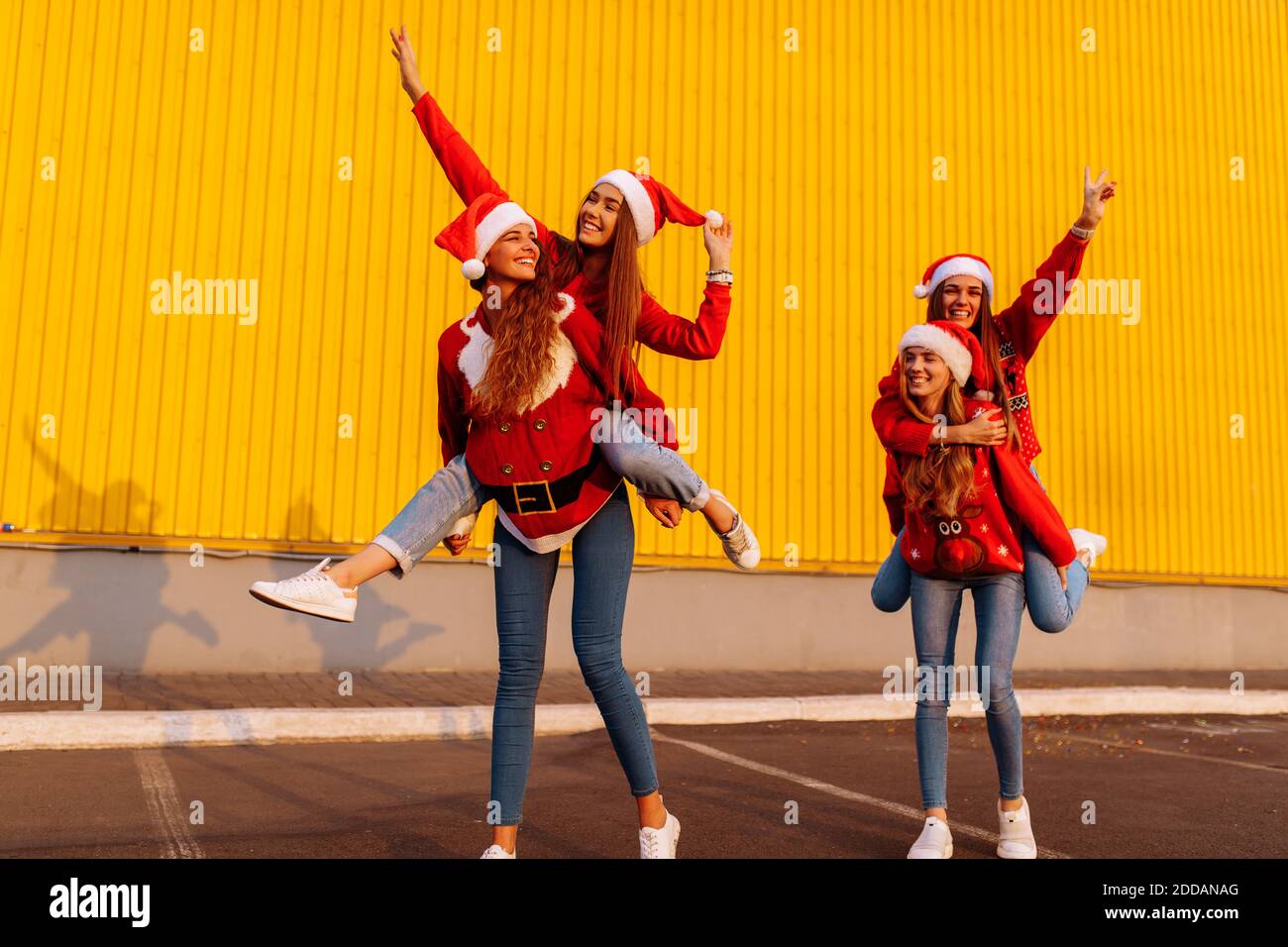 Gruppe von glücklichen Freunden tragen weihnachtsmann Hüte haben Spaß Und reiten sich gegenseitig in der frischen Luft gegen ein Gelbe Wand Stockfoto