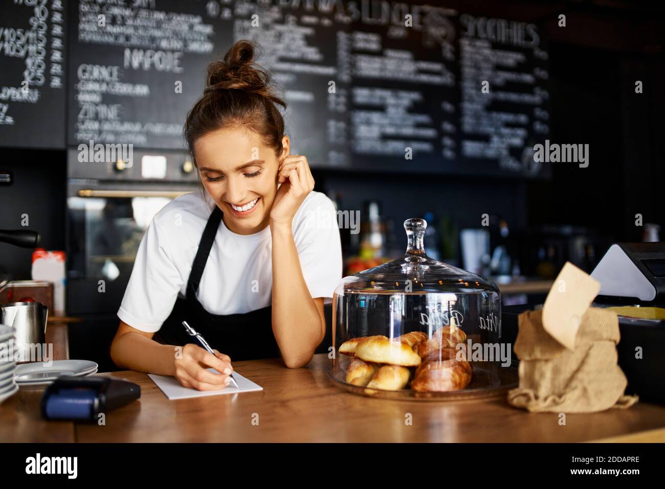 Lächelnder Barista, der während der Arbeit im Café auf dem Notizblock schreibt Stockfoto