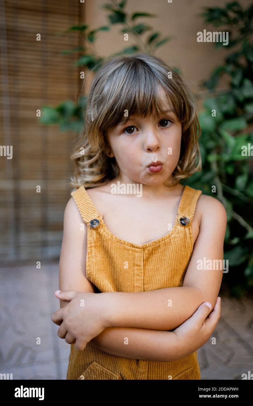 Mädchen, das Gesicht macht, während sie zu Hause mit gekreuzten Armen steht Stockfoto