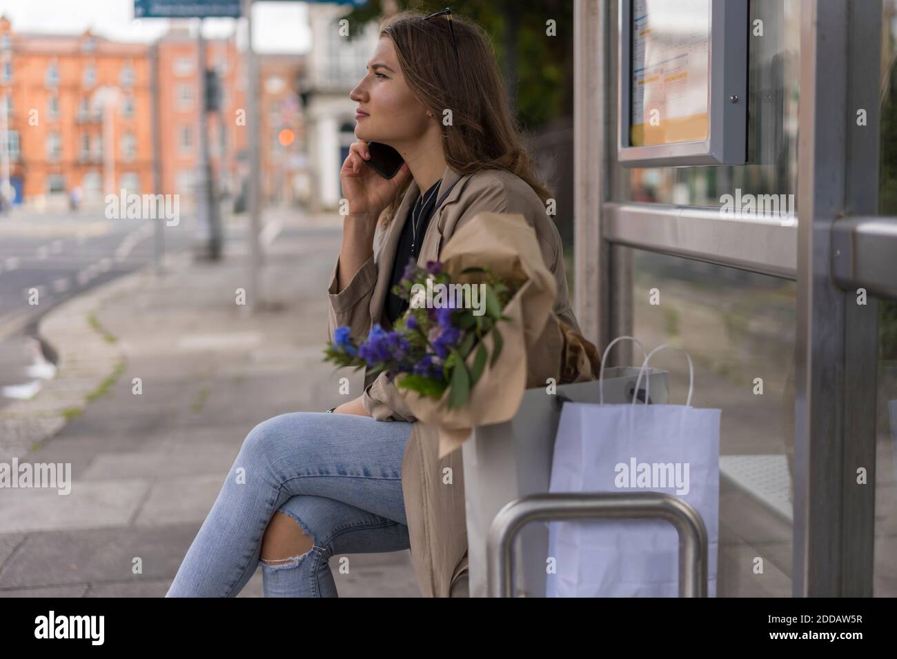 Junge Frau im Gespräch auf Smartphone mit Einkaufstaschen während Sitzen in der Stadt Stockfoto