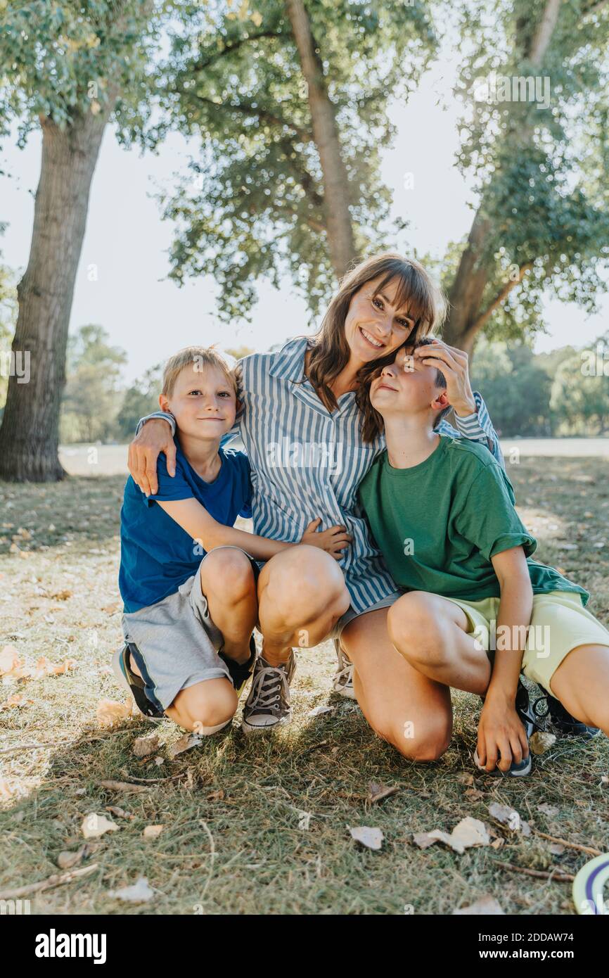 Glückliche Mutter umarmt Söhne während kniete im öffentlichen Park auf Sonniger Tag Stockfoto