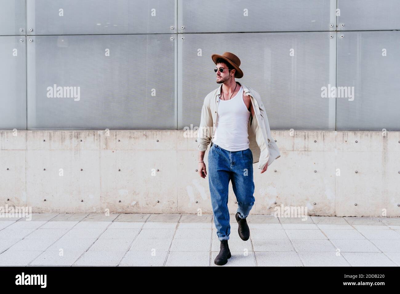 Selbstbewusster Mann im Hut schaut weg, während er gegen die Wand läuft Stockfoto