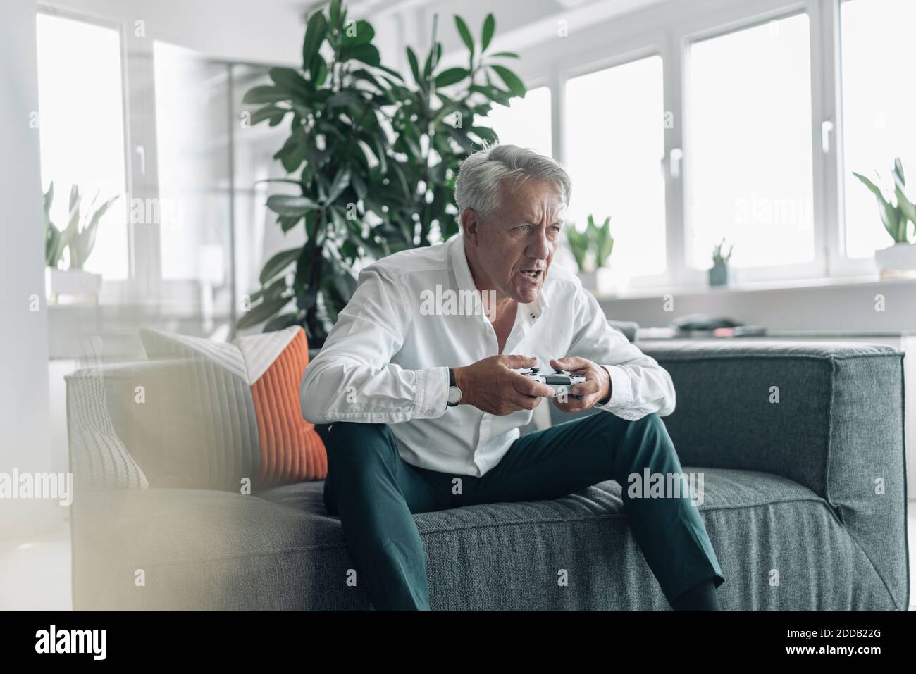 Senior Geschäftsmann spielt Videospiel mit Konzentration, während Sie sitzen auf Sofa im Büro Stockfoto