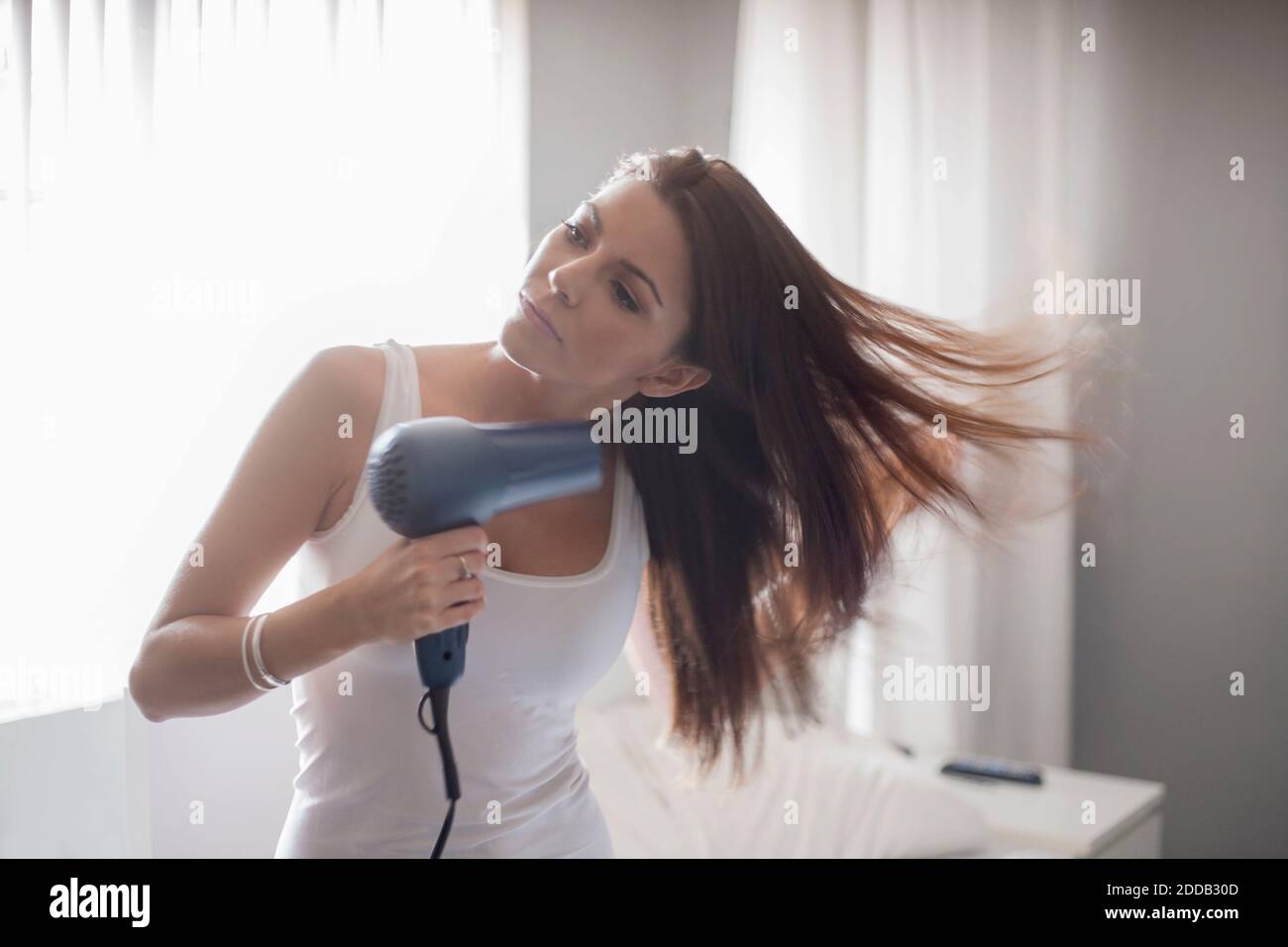 Junge Frau, die Haare trocknet, während sie zu Hause im Schlafzimmer steht Stockfoto