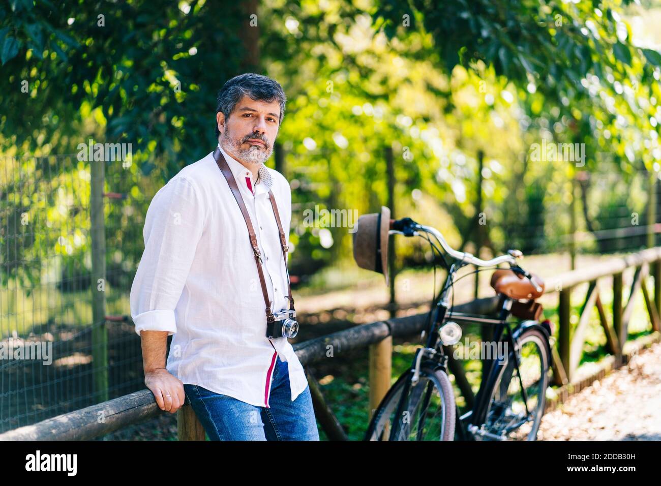 Reifer Mann mit Kamera um den Hals lehnt auf Holzstruktur Im Park Stockfoto