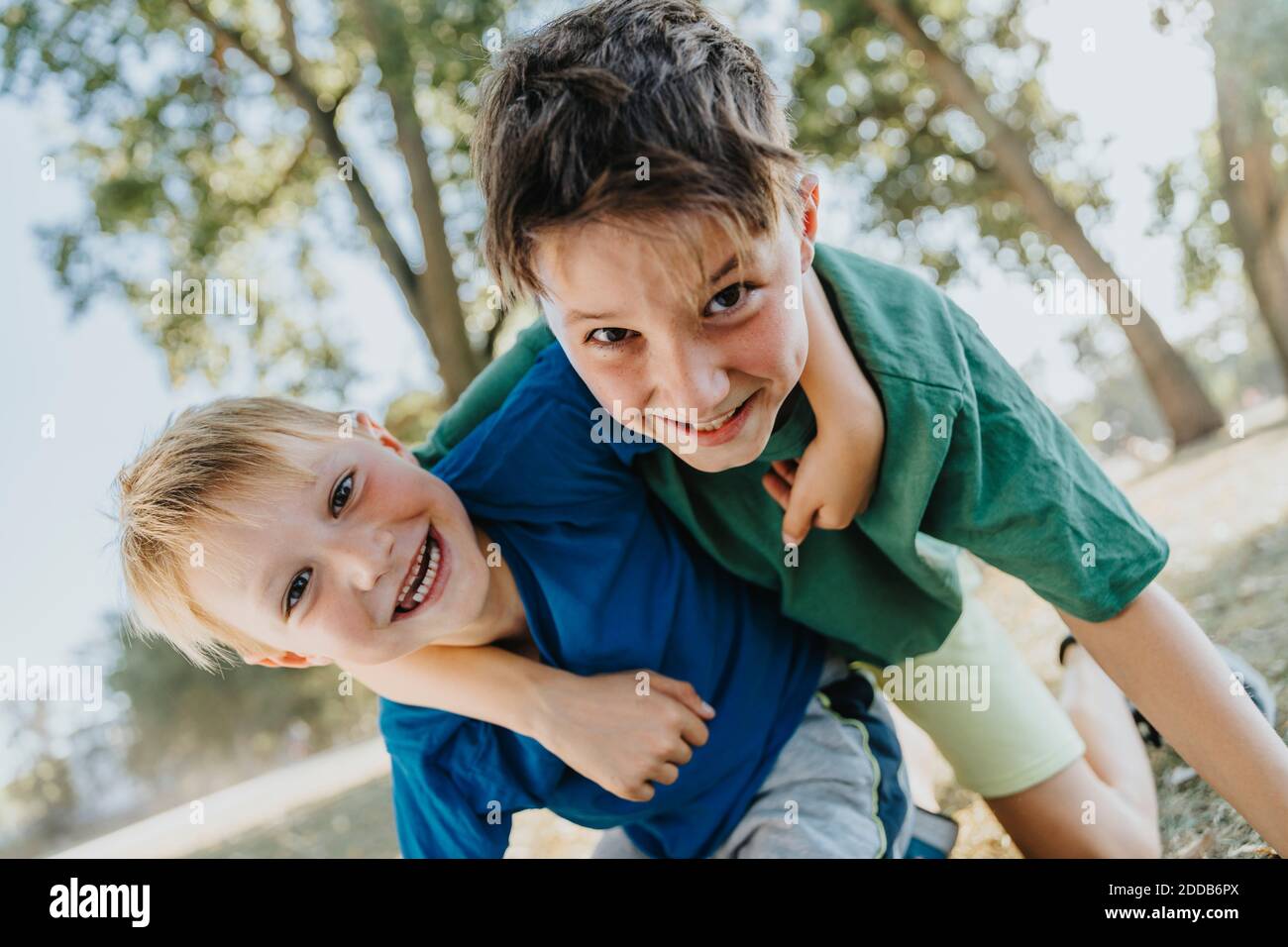Lächelnde Brüder mit Arm um die Knie im öffentlichen Park auf Sonniger Tag Stockfoto