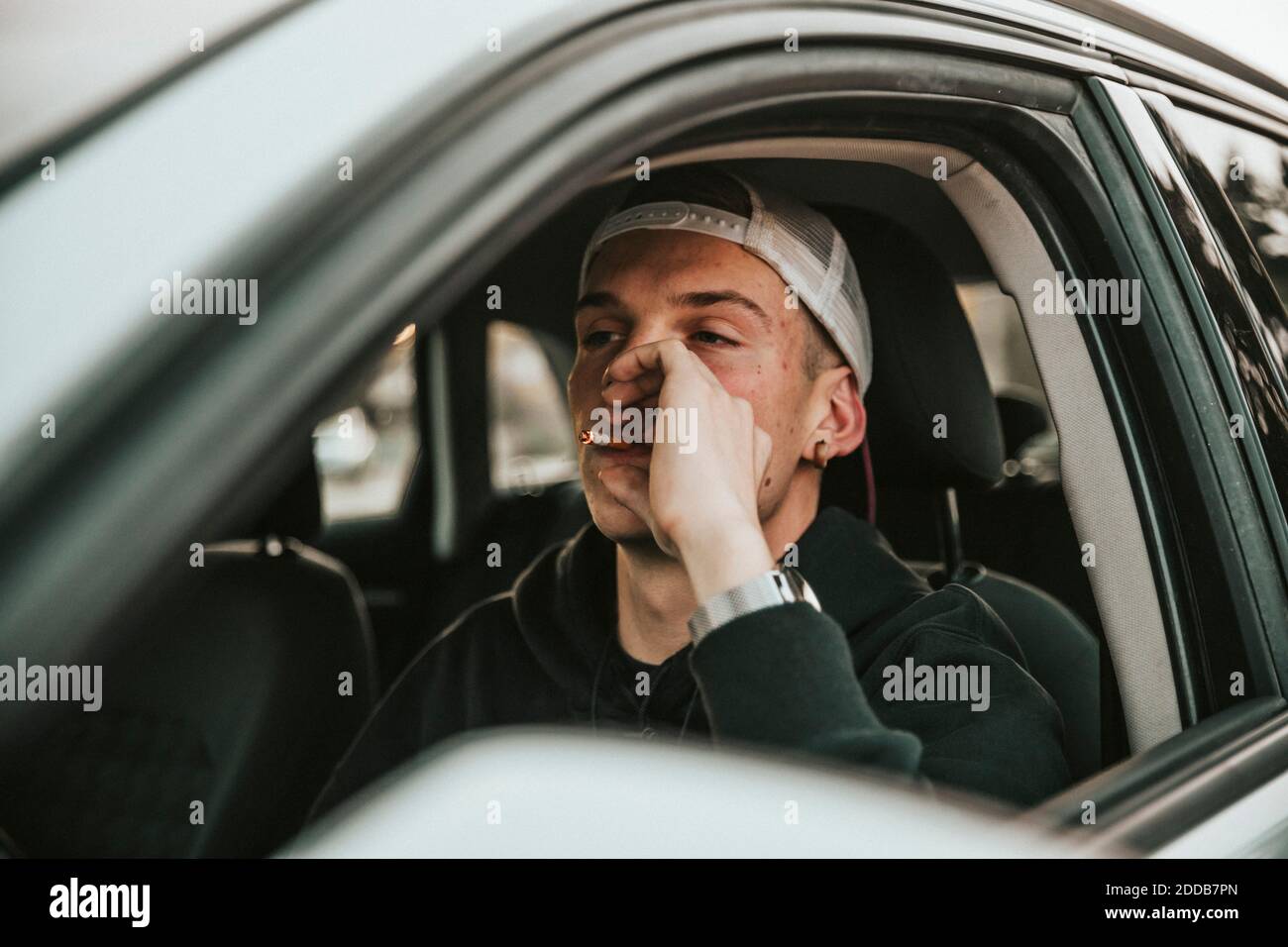 Junger Mann raucht Zigarette, während er Auto fährt Stockfoto