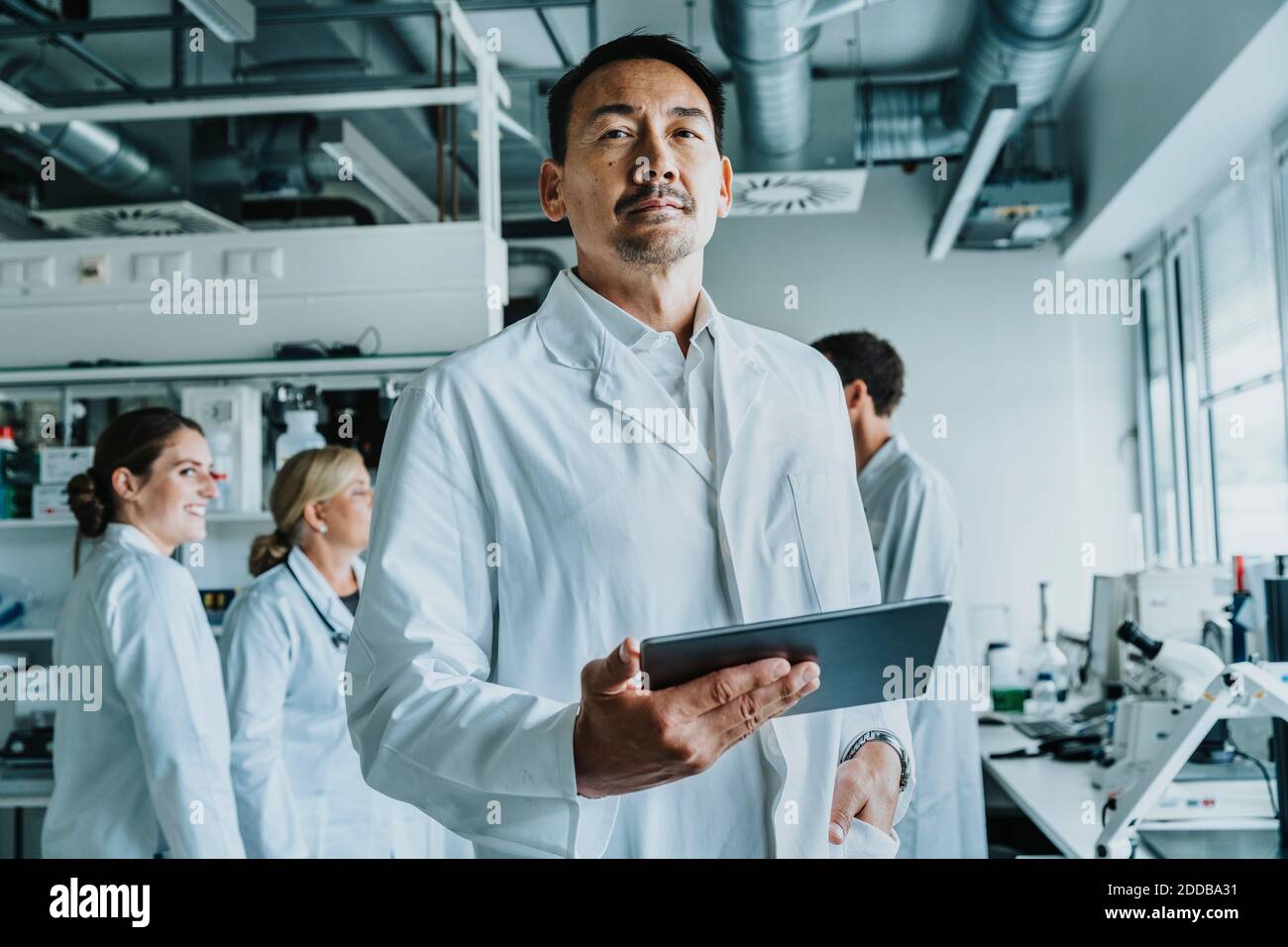Wissenschaftler mit der Hand in der Tasche und digitale Tablet stehen mit Mitarbeiter im Hintergrund im Labor Stockfoto