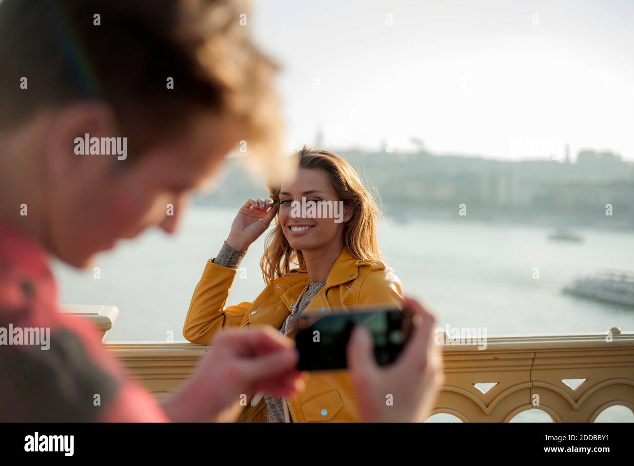 Junger Mann fotografiert junge Frau mit Smartphone Auf Brücke gegen Himmel Stockfoto