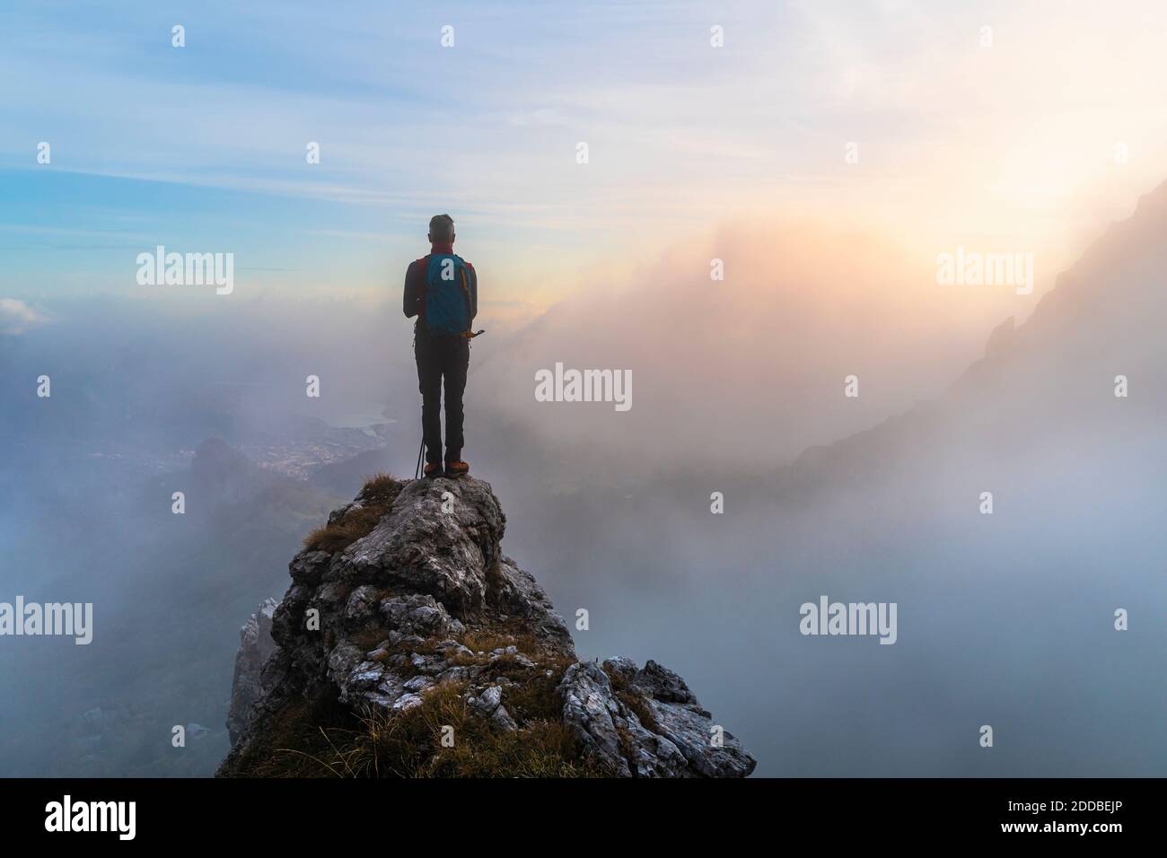 Nachdenklicher männlicher Wanderer, der während des Sonnenaufgangs auf Bergamasque Alps, Italien, auf dem Berggipfel steht Stockfoto