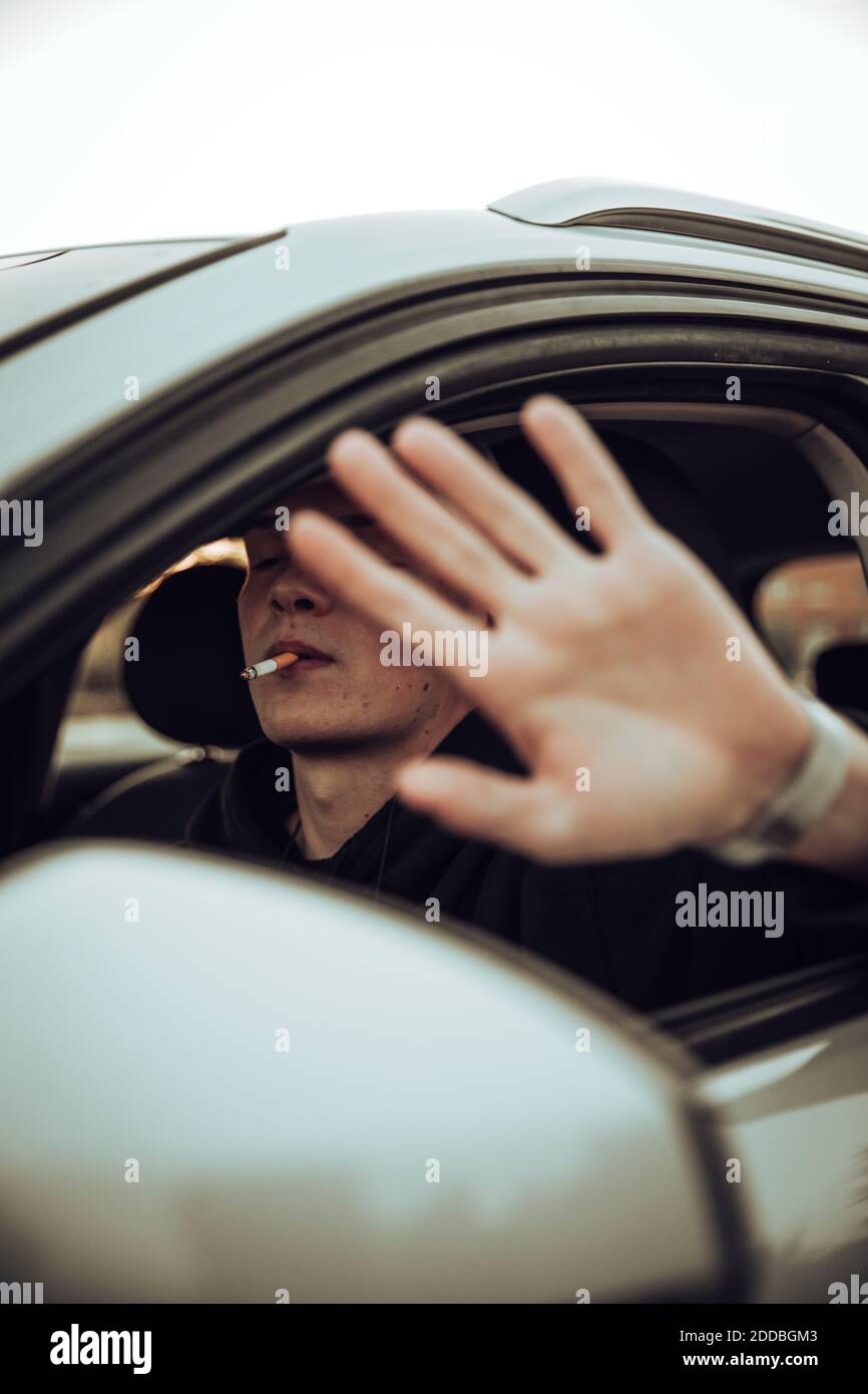 Junger Mann mit Stop-Geste, während er im Auto Zigarette raucht Stockfoto