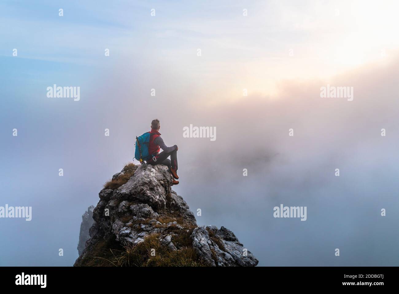Nachdenklicher männlicher Wanderer, der während des Sonnenaufgangs auf Bergamasque Alps, Italien, auf dem Berggipfel sitzt Stockfoto