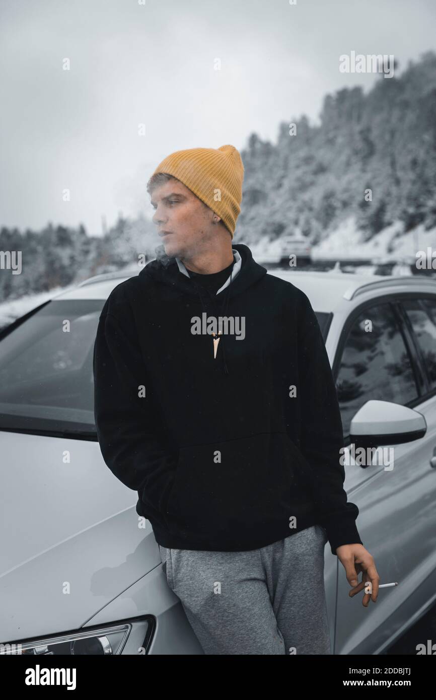 Junger Mann raucht während er sich im Winter auf das Auto stützt Stockfoto