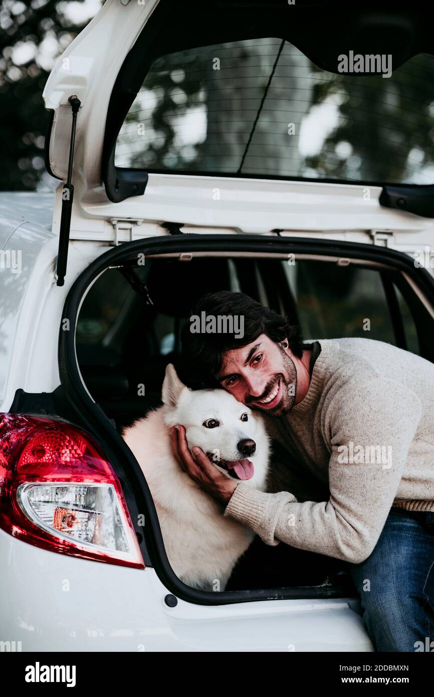 Lächelnder Mann umarmt Hund, während er im Kofferraum sitzt Wald Stockfoto
