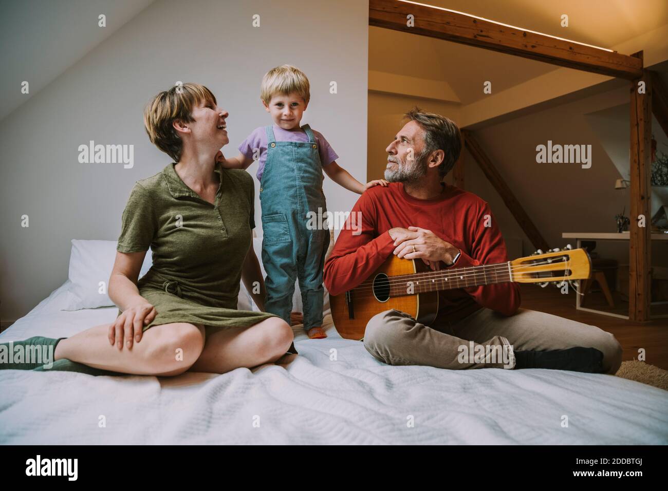 Sohn, der zwischen Mutter und Vater steht und Gitarre spielt Zu Hause im Schlafzimmer Stockfoto