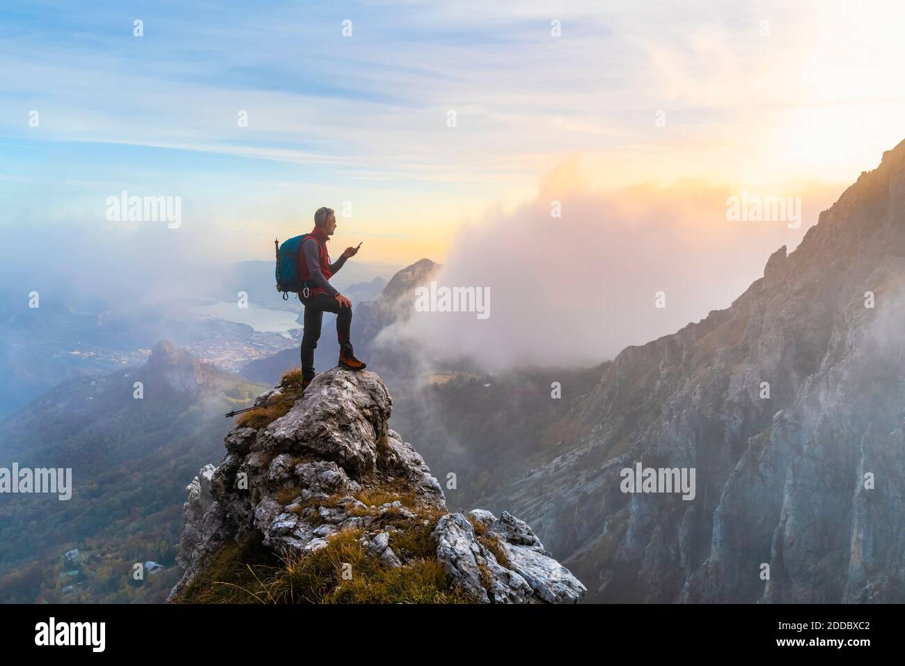 Nachdenkliche Wanderer mit Smartphone auf Berggipfel während Sonnenaufgang in Bergamasque Alpen, Italien Stockfoto