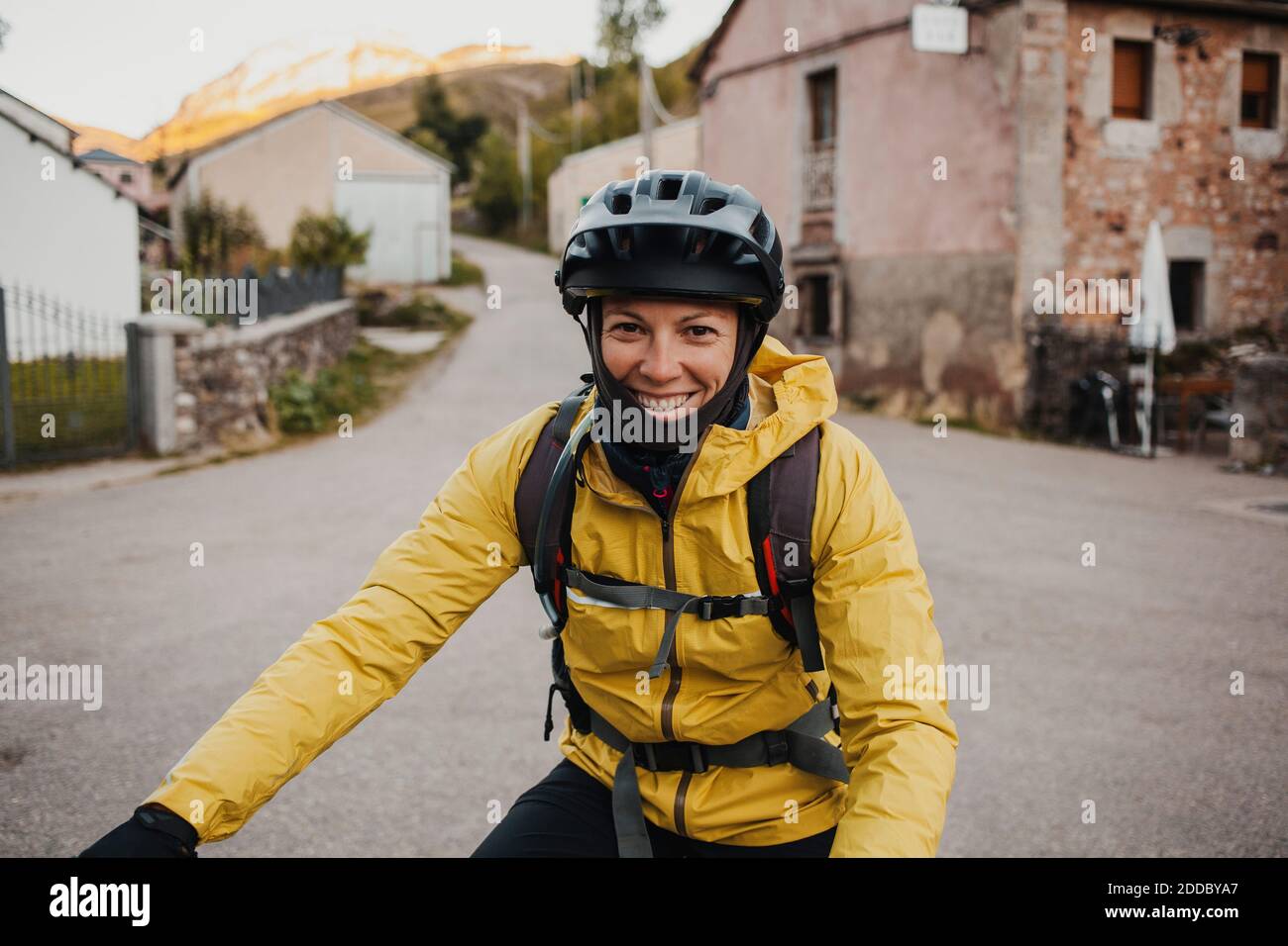 Lächelnde Frau mittleren Erwachsenen in warmer Kleidung Reiten Mountainbike auf der Straße während der Reise zum Somiedo Naturpark, Spanien Stockfoto