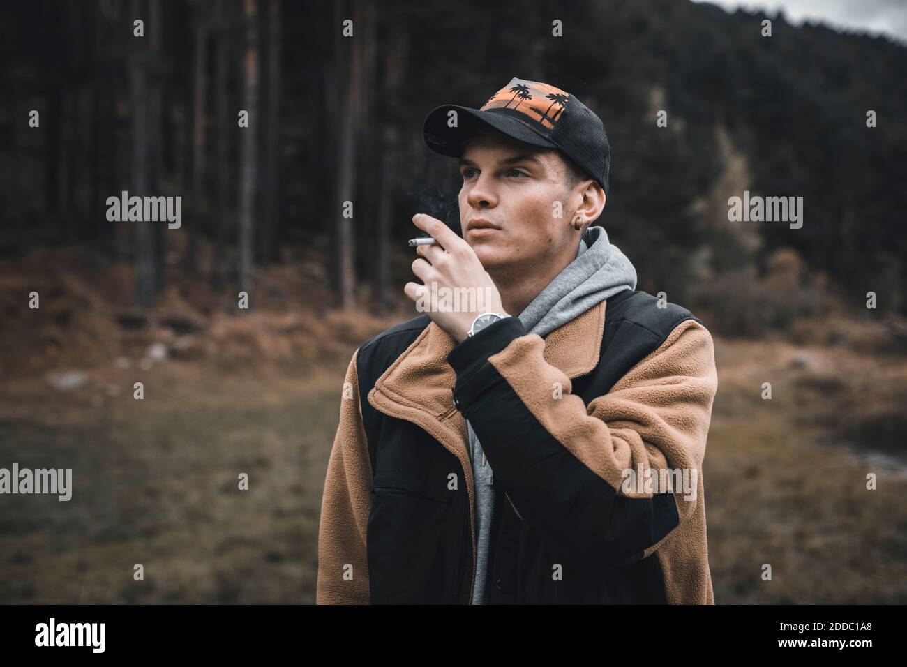 Junger Mann, der beim Rauchen im Wald steht, während er wegschaut Herbst Stockfoto