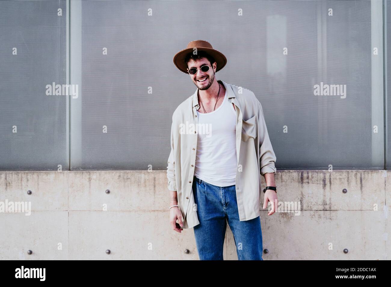Lächelnder Mann im Hut schaut weg, während er gegen die Wand steht Stockfoto