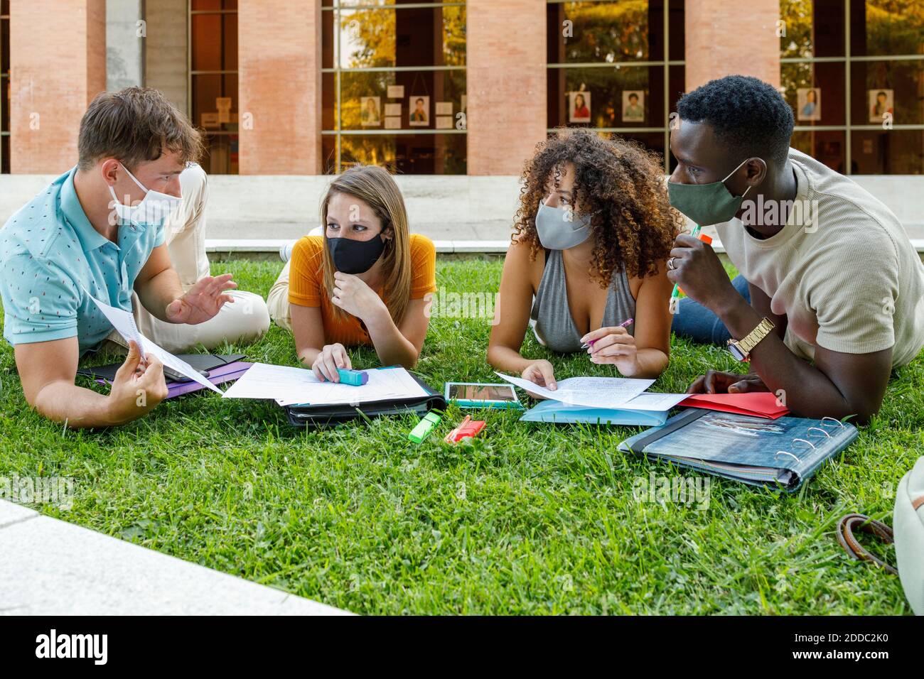 Männliche und weibliche Schüler tragen Sicherheitsmaske während der Diskussion auf Gras auf dem Universitätscampus Stockfoto