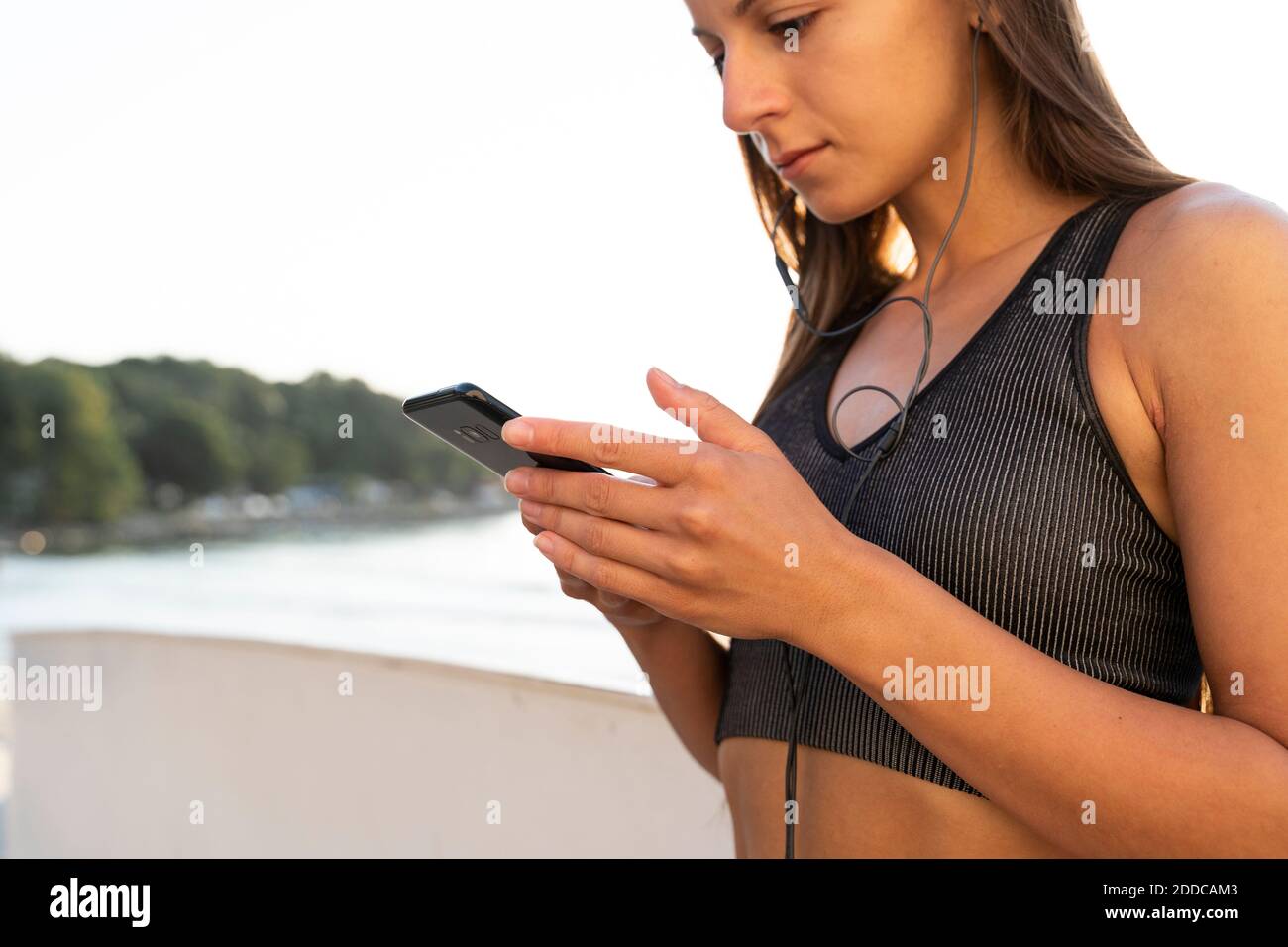 Fitness Frau Musik hören über Kopfhörer mit Smartphone, während Stehen gegen Meer bei Sonnenaufgang Stockfoto