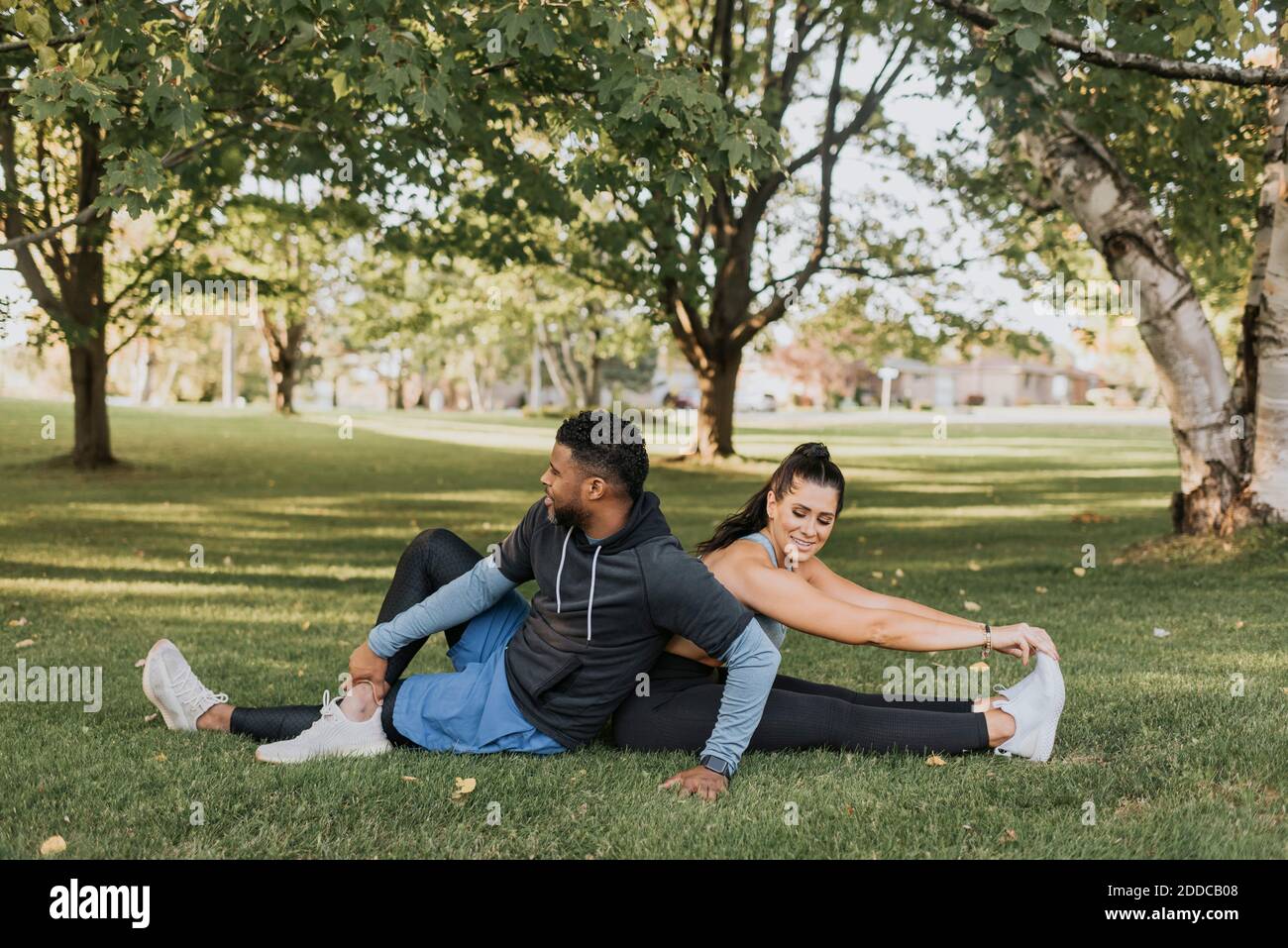 Pärchen macht Aufwärm-Übung, während sie im Hinterhof sitzen Stockfoto